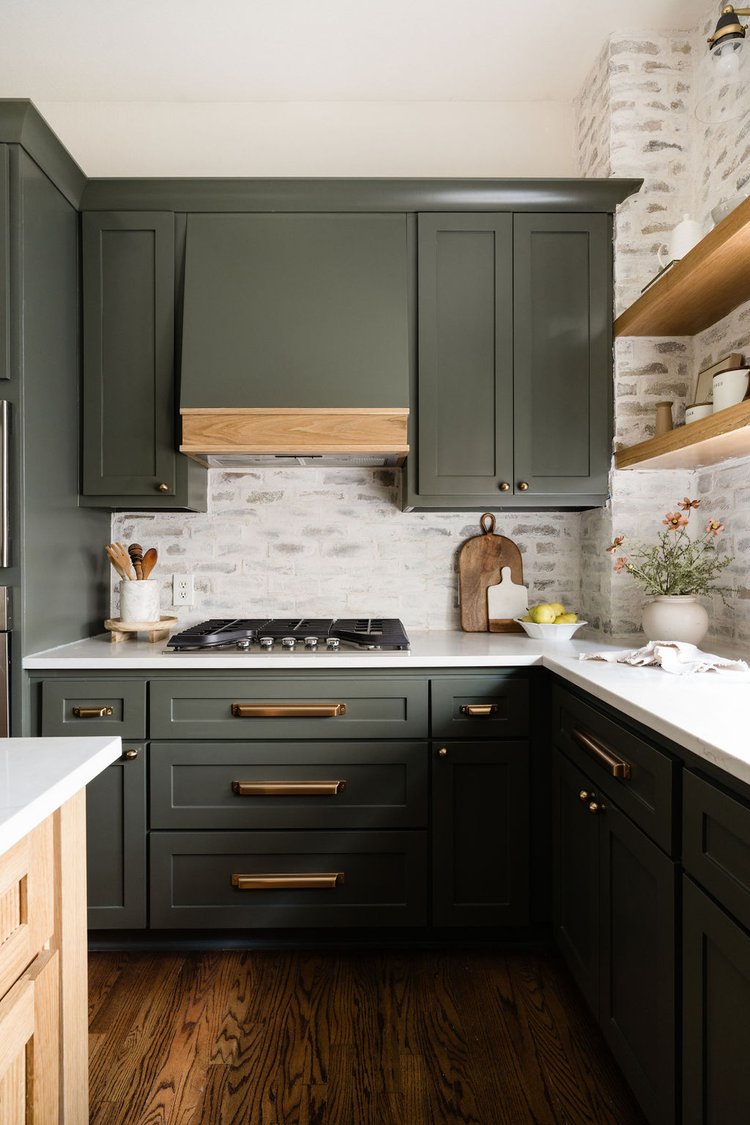 Dark green kitchen cabinetry, range hood, and brass pulls