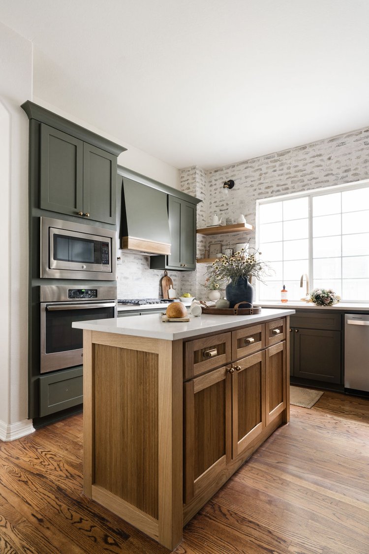 Oak island with a white worktop beside dark green cabinetry